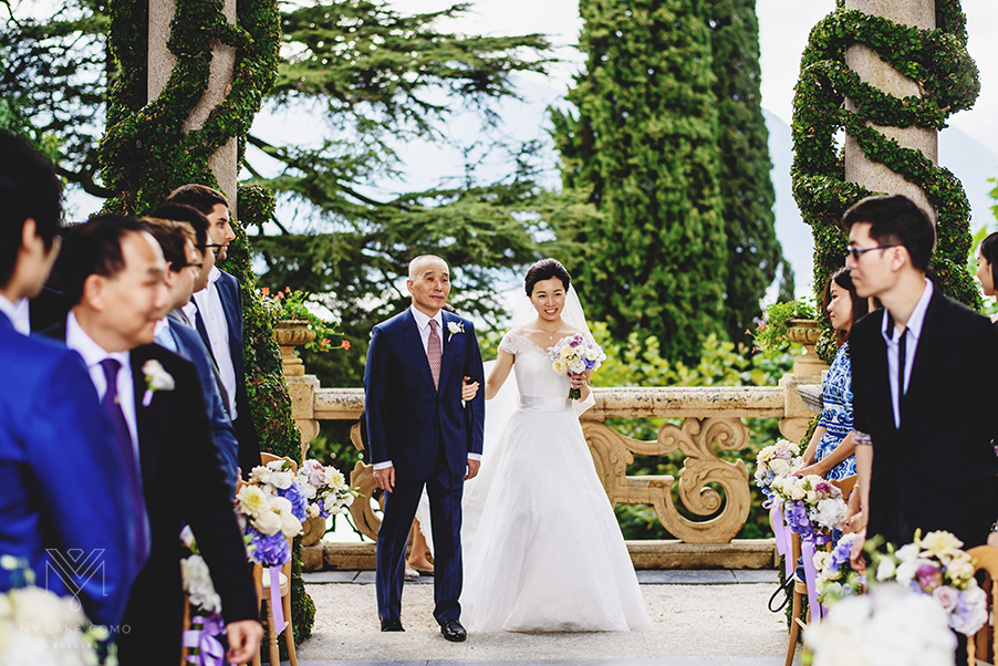 Bride-and-father-enter-wedding-ceremony-terrace-on-Lake-Como-at-Villa-Balbianello